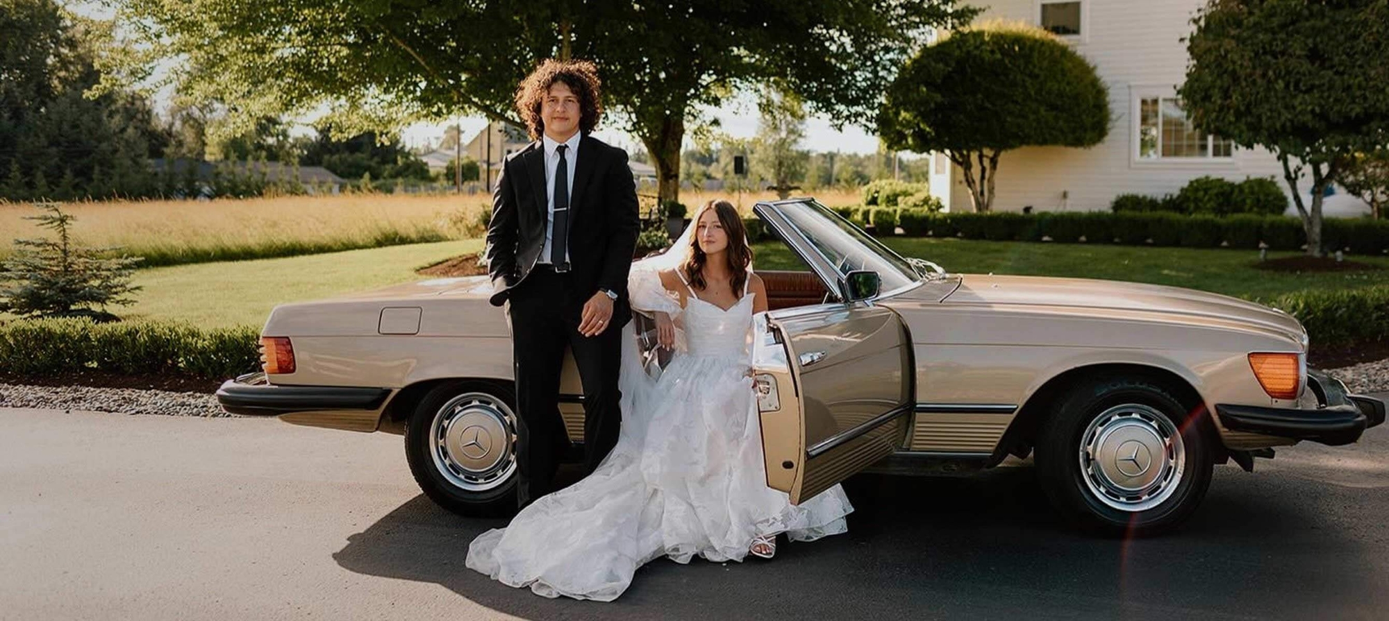 Сouple wearing a white gown and a black suit near a car